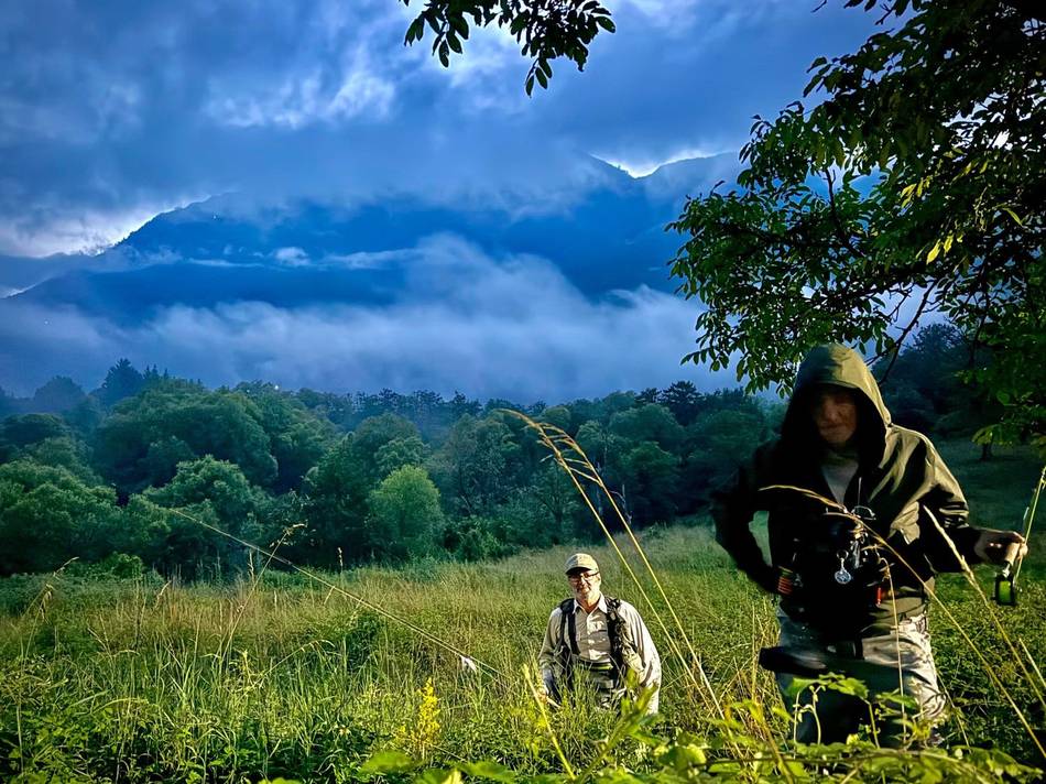 Two anglers walking through a meadow under storm clouds