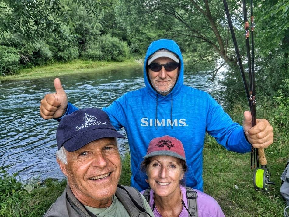 Three anglers smiling by the river, thumbs up