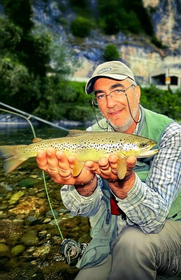 An angler with a brown trout in clear water