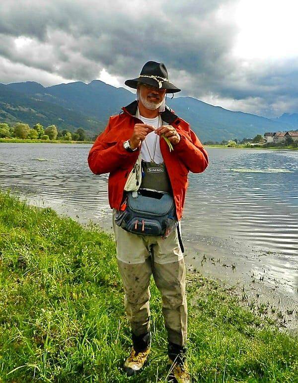 An angler in a red jacket by the lake with the mountains behind