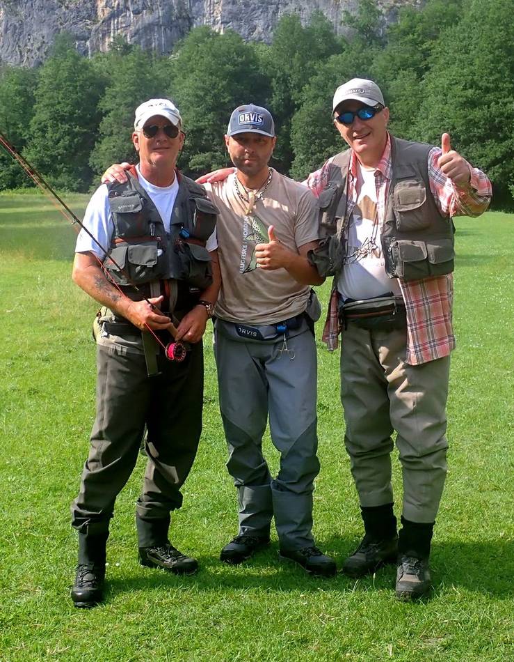 Three anglers on the meadow below a rock wall, thumbs up