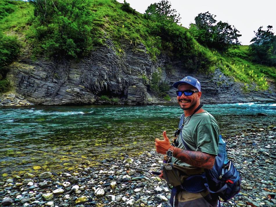 A smiling angler giving a thumbs up by the turquoise river