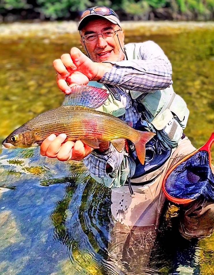 An angler holding a grayling in the river