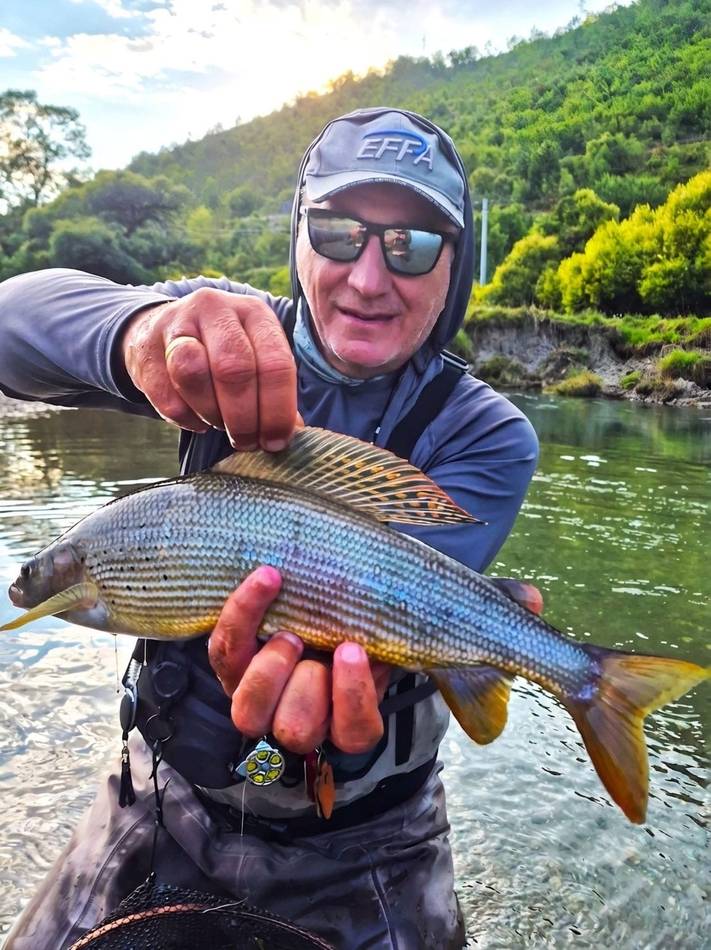 An angler holding a grayling caught on the river at sunrise