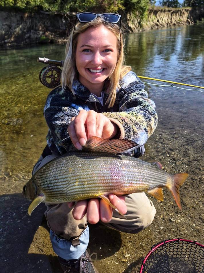 A guest smiling with her grayling catch by the river