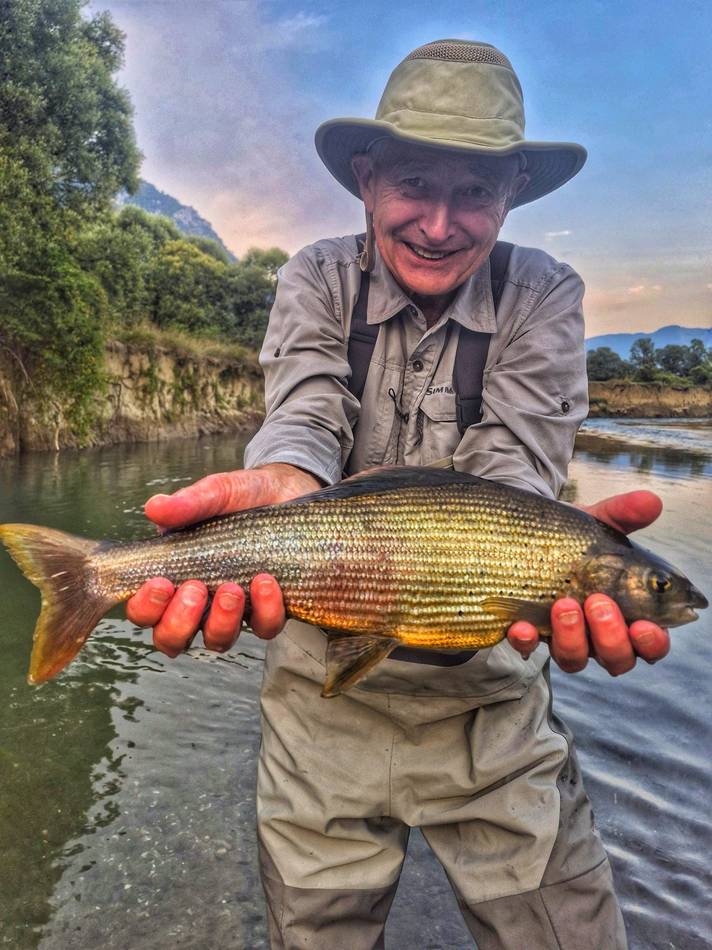 A guest holding his grayling catch at dusk, mountains behind