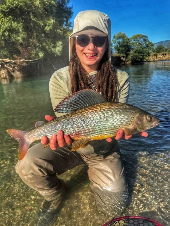 A guest kneeling with her grayling catch in the shallows