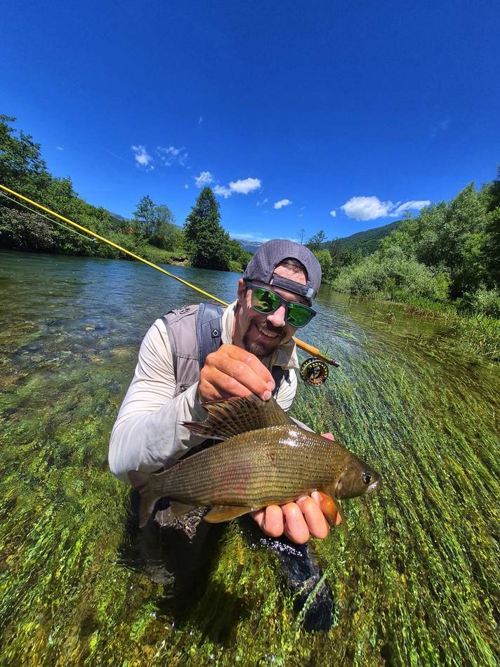 A guest holding his grayling by a calm green pool