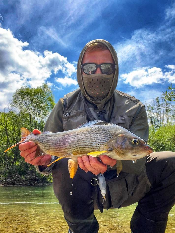 A masked guest holding his colourful grayling catch