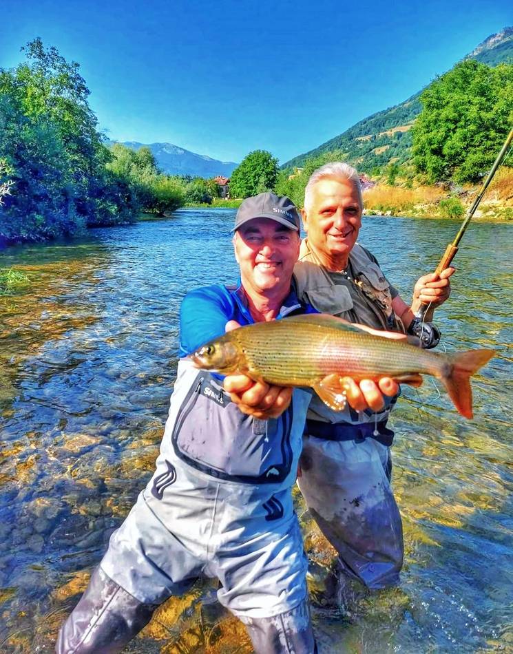 A guest holding his grayling with the mountains behind