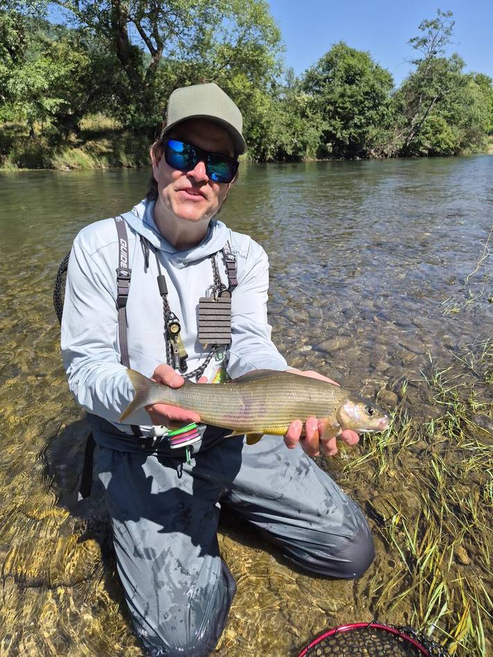 A guest holding his grayling by the riverside