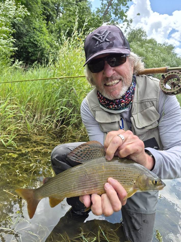 A guest smiling with his grayling catch by the reeds