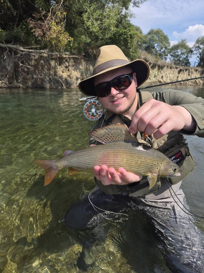 A guest holding his grayling by the riverside